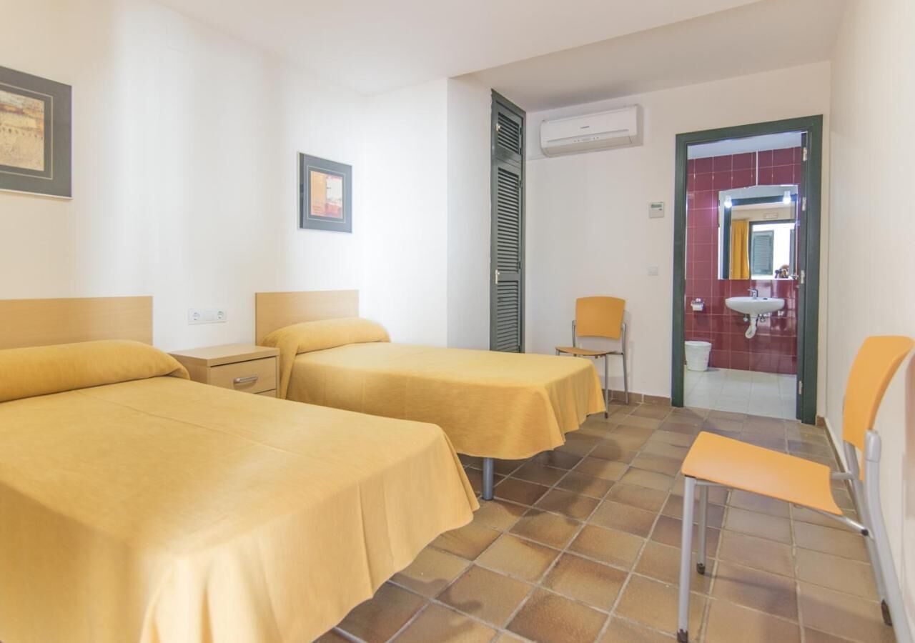 Habitación de hotel con dos camas, una silla, una mesita y un baño visible a través de una puerta abierta.