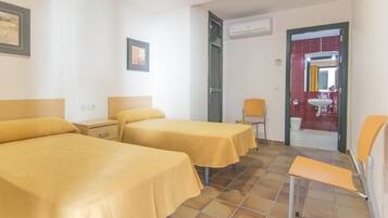 Habitación de hotel con dos camas, una silla, una mesita y un baño visible a través de una puerta abierta.