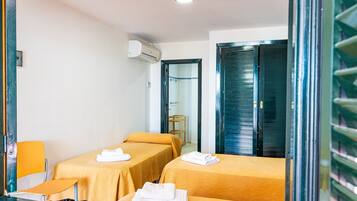 Habitació d'hotel amb dos llits individuals, una taula petita, una cadira, un aparell d'aire condicionat i una porta amb mànec metàl·lic.