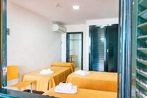 A hotel room with two single beds, a small table, a chair, an air conditioning unit, and a door with a metal handle. - Albergue Inturjoven Punta Umbria - Hostel (Punta Umbría)