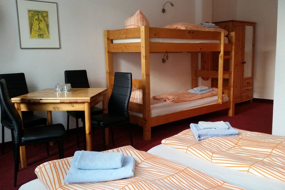 Una cama litera con ropa de cama a rayas anaranjadas, una mesa de madera con sillas y un mueble pequeño.