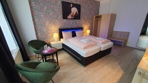 A bedroom with a bed, bedside lamps, a chair, a small table, and a wardrobe. - Bornholmer Hof (Berlin)