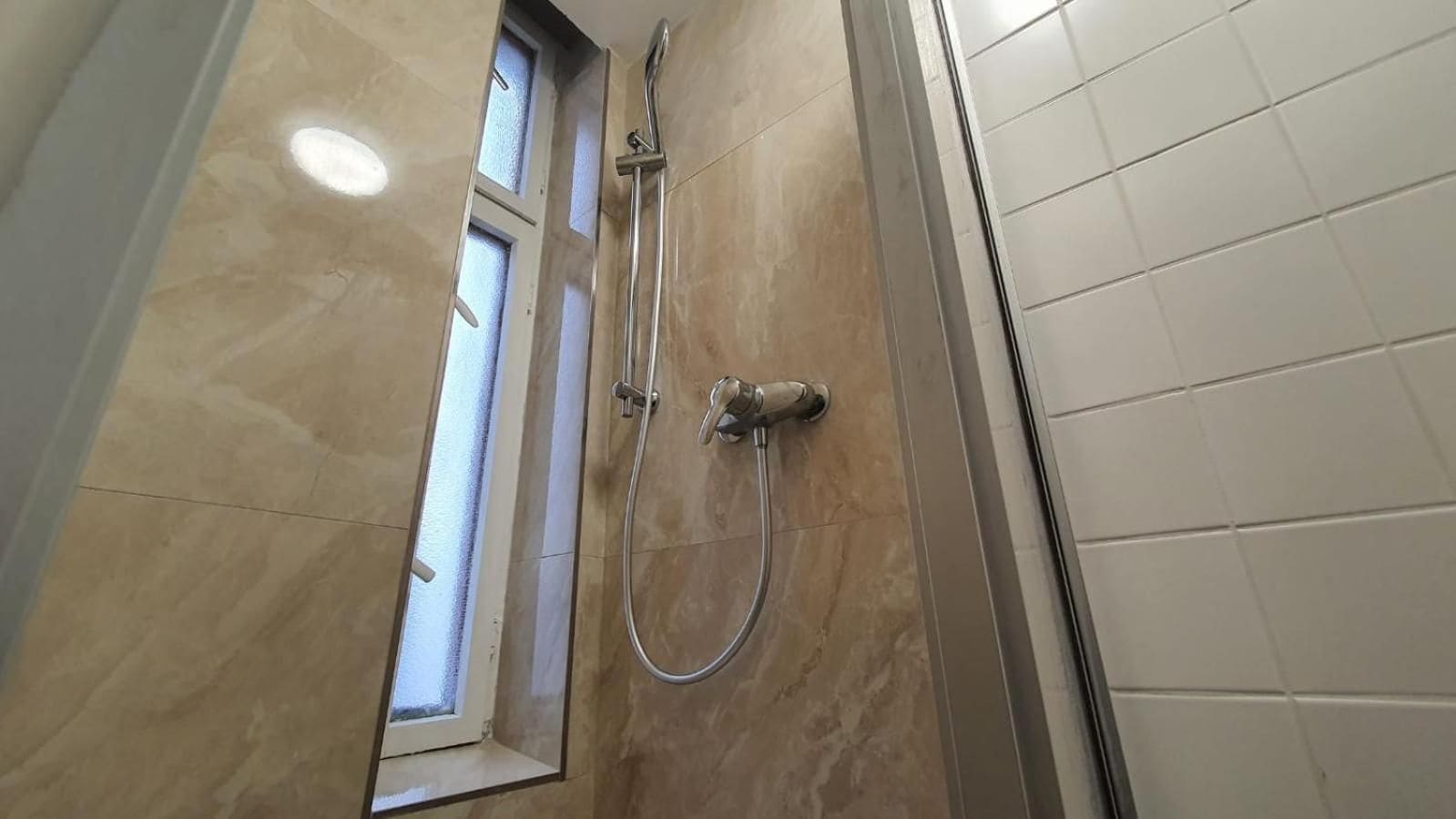 Ein Badezimmer mit Dusche, Fenster und Fliesenwänden.