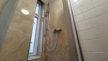 Ein Badezimmer mit Dusche, Fenster und Fliesenwänden.