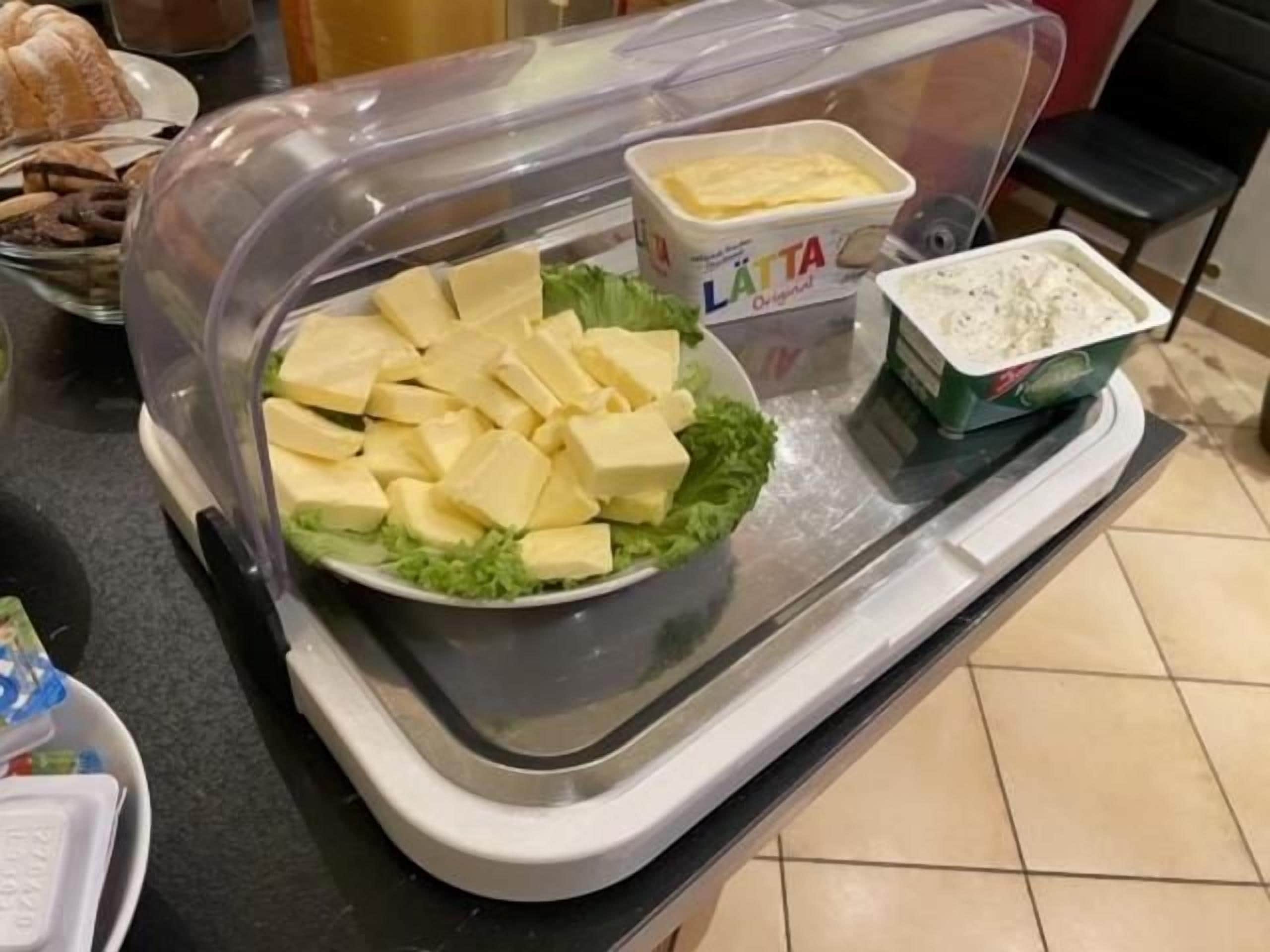 Montaje tipo buffet con diversos alimentos, incluyendo un bol de queso en cubos, un recipiente con aderezo para ensalada y un recipiente con yogur.
