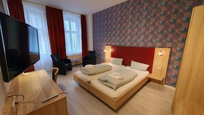 Una habitación de hotel moderna con una cama grande, un televisor, un escritorio con una silla y una ventana con cortinas.