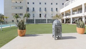 Een modern gebouw met een plat dak, meerdere balkons en een binnentuin met kunstgras en potplanten.