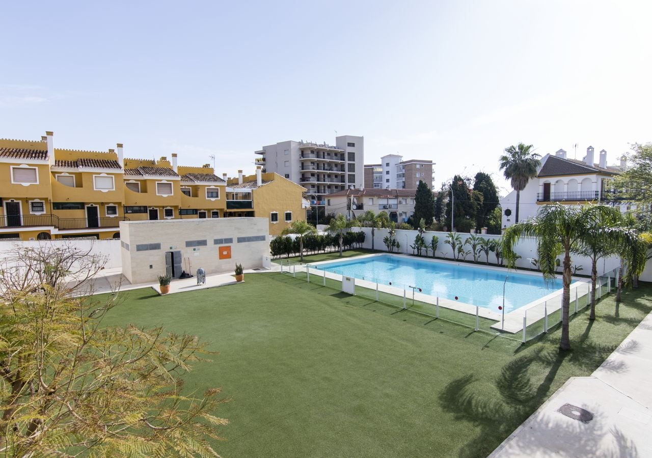Una piscina rodeada de césped verde, con edificios al fondo.