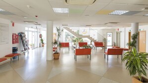 Een ruime lobby met een trap, rode zitplaatsen en potplanten.