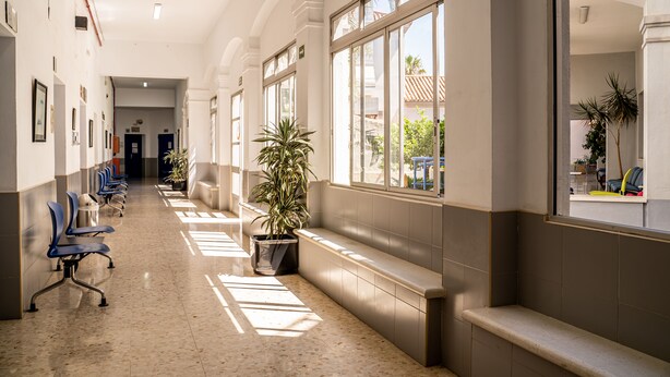 A long, well-lit hallway with rows of blue chairs, potted plants, and large windows offering views of the outdoors. - Albergue Inturjoven Málaga - Hostel (Málaga)