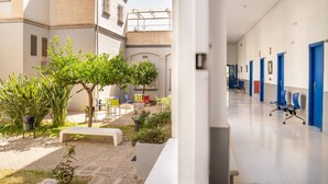 A corridor with blue doors, a bench, and outdoor seating area with plants and chairs. - Albergue Inturjoven Málaga - Hostel (Málaga)
