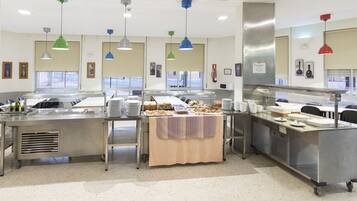 A spacious kitchen with stainless steel counters, multiple food stations, and hanging pendant lights.