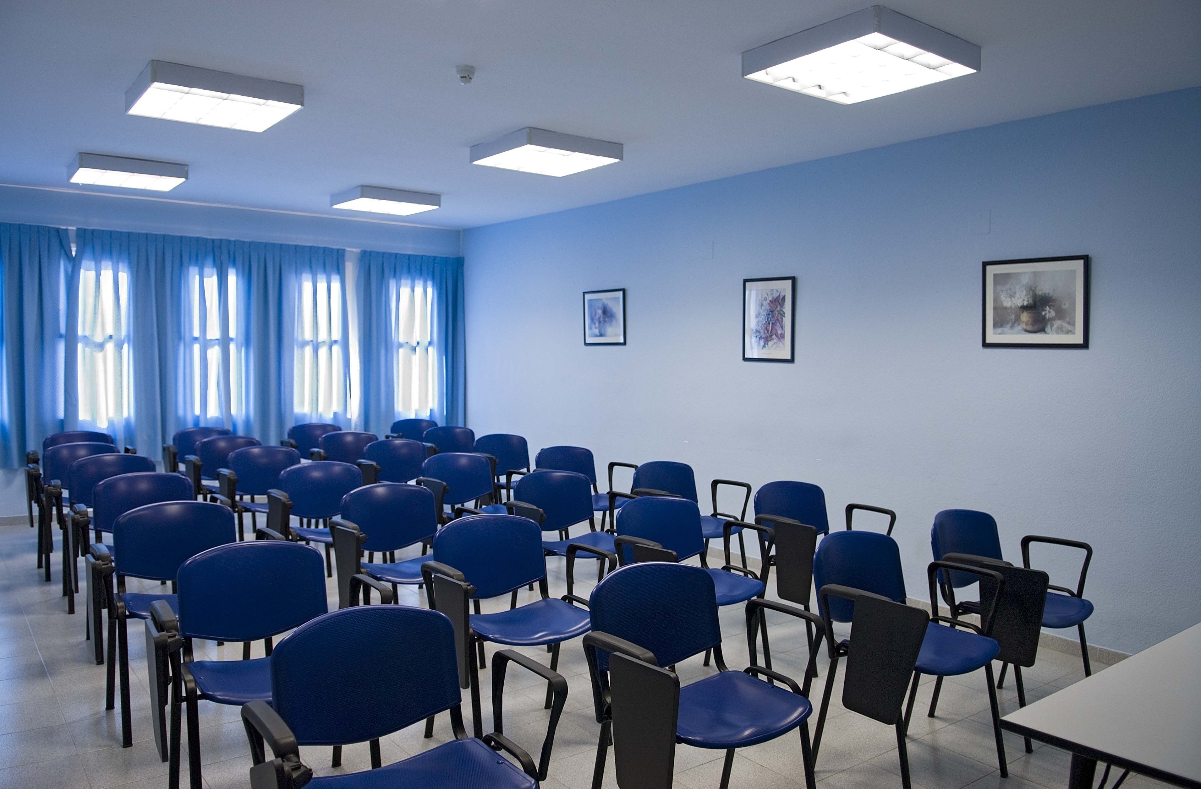 A conference room with rows of blue chairs, a white table, and blue curtains.
