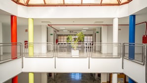 Un atrio de varios niveles con una escalera central, barandillas de metal y una planta en maceta.