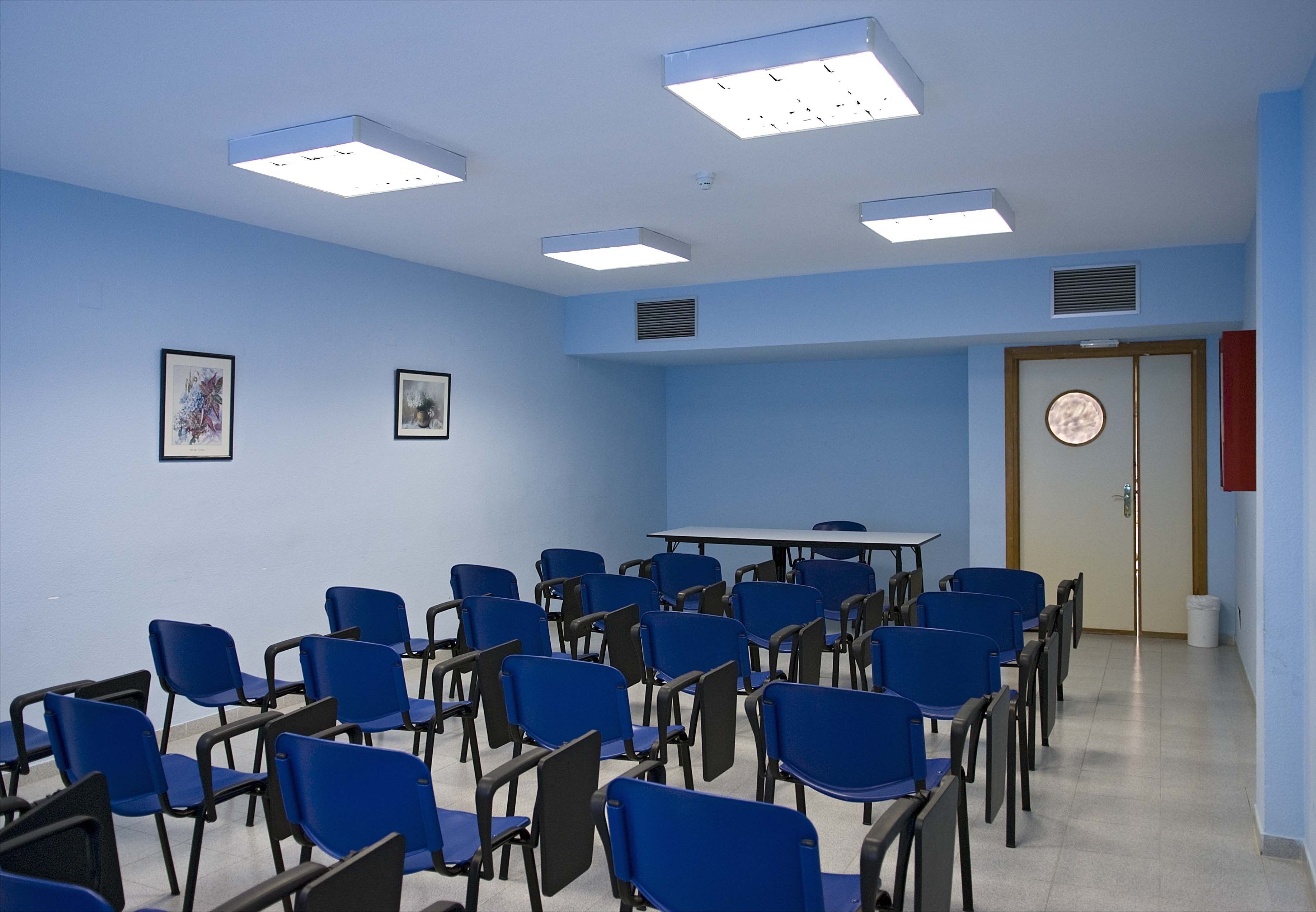Una sala de conferencias con sillas azules, una mesa y luces en el techo.