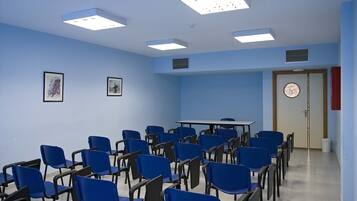Una sala de conferencias con sillas azules, una mesa y luces en el techo.