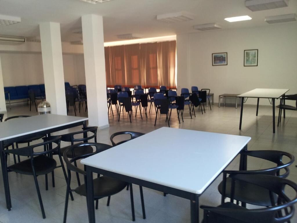 Un salón de conferencias con mesas y sillas, un ventanal con cortinas y cuadros en la pared.