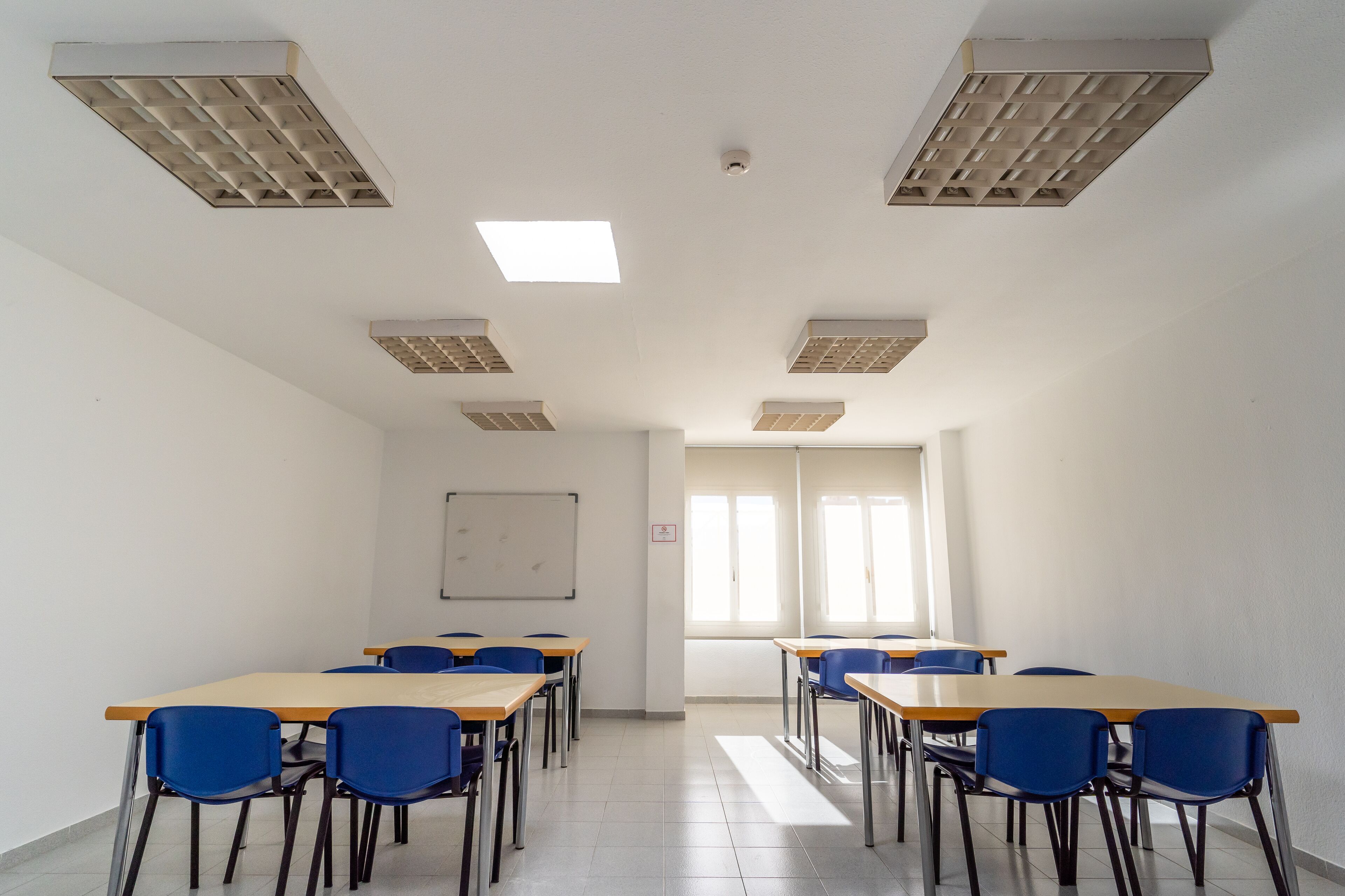 A classroom with desks and chairs, whiteboard, and windows.