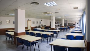 A cafeteria with multiple tables and chairs, a tiled floor, and ceiling lights. - Albergue Inturjoven Almería - Hostel (Almeria)