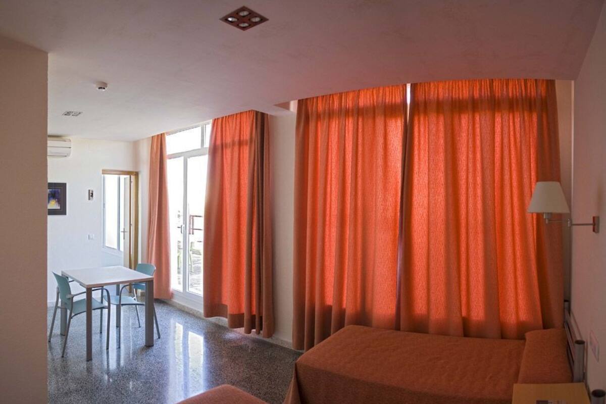 Habitación de hotel con dos camas, una mesa, sillas y una lámpara.