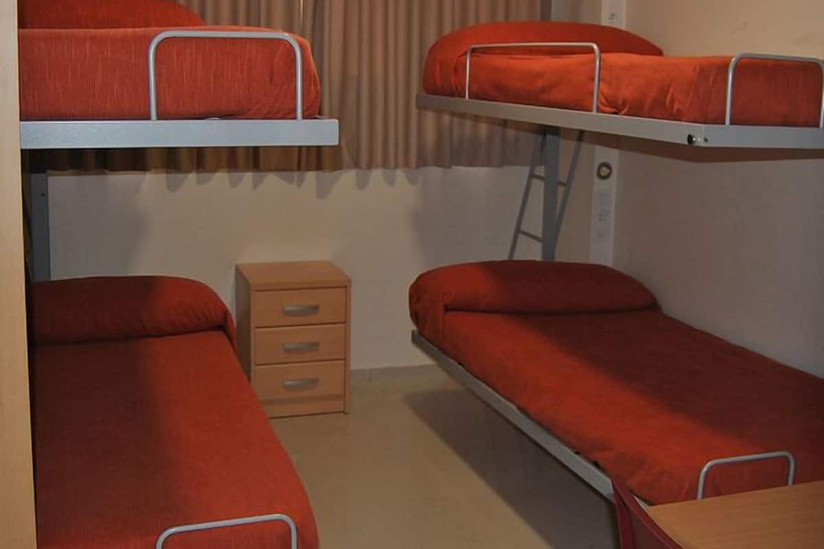 Un dormitorio con literas, un pequeño aparador de madera y una ventana con cortinas.