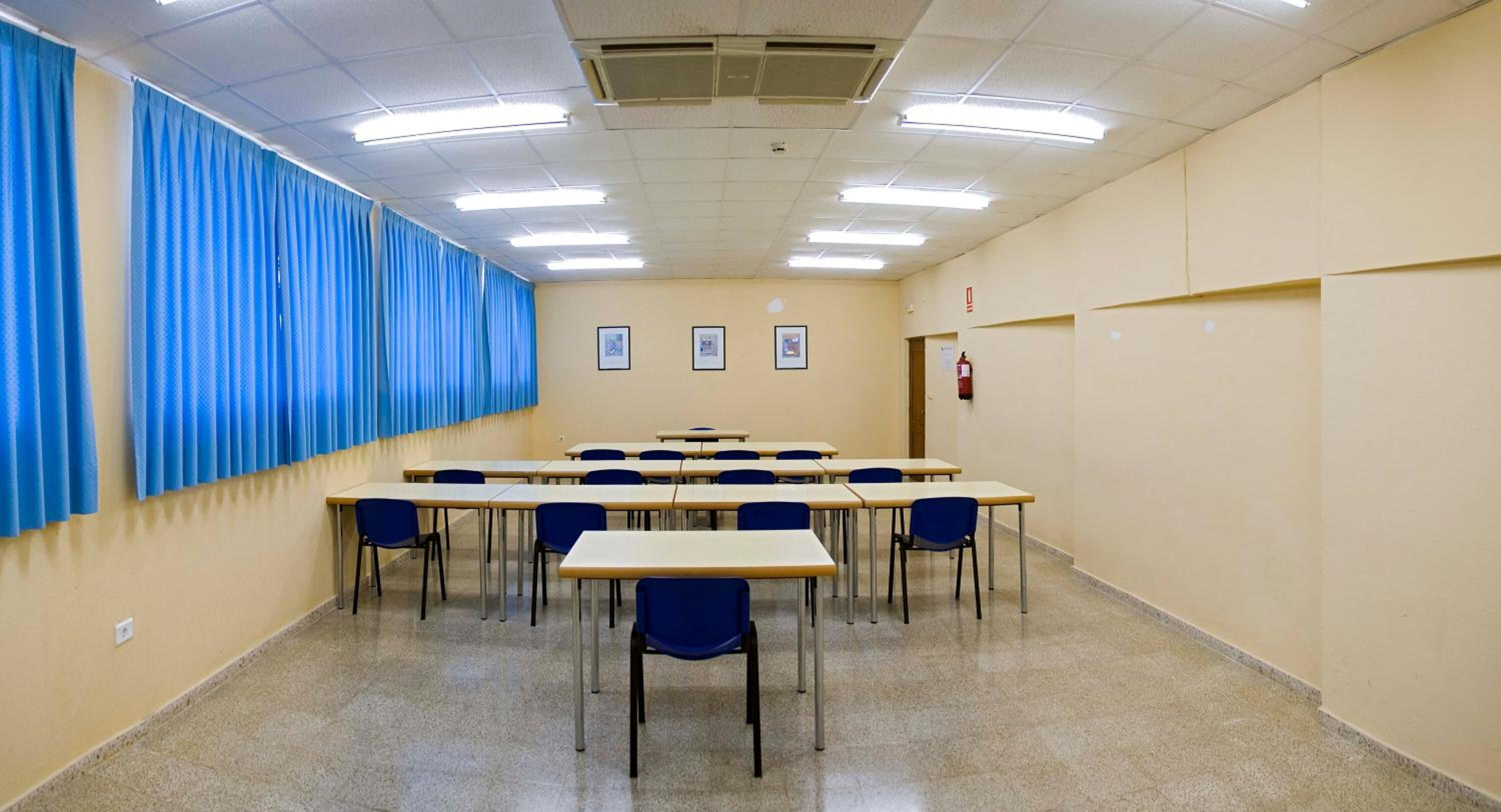 A conference room with tables and chairs, a fire extinguisher, and framed pictures on the wall.