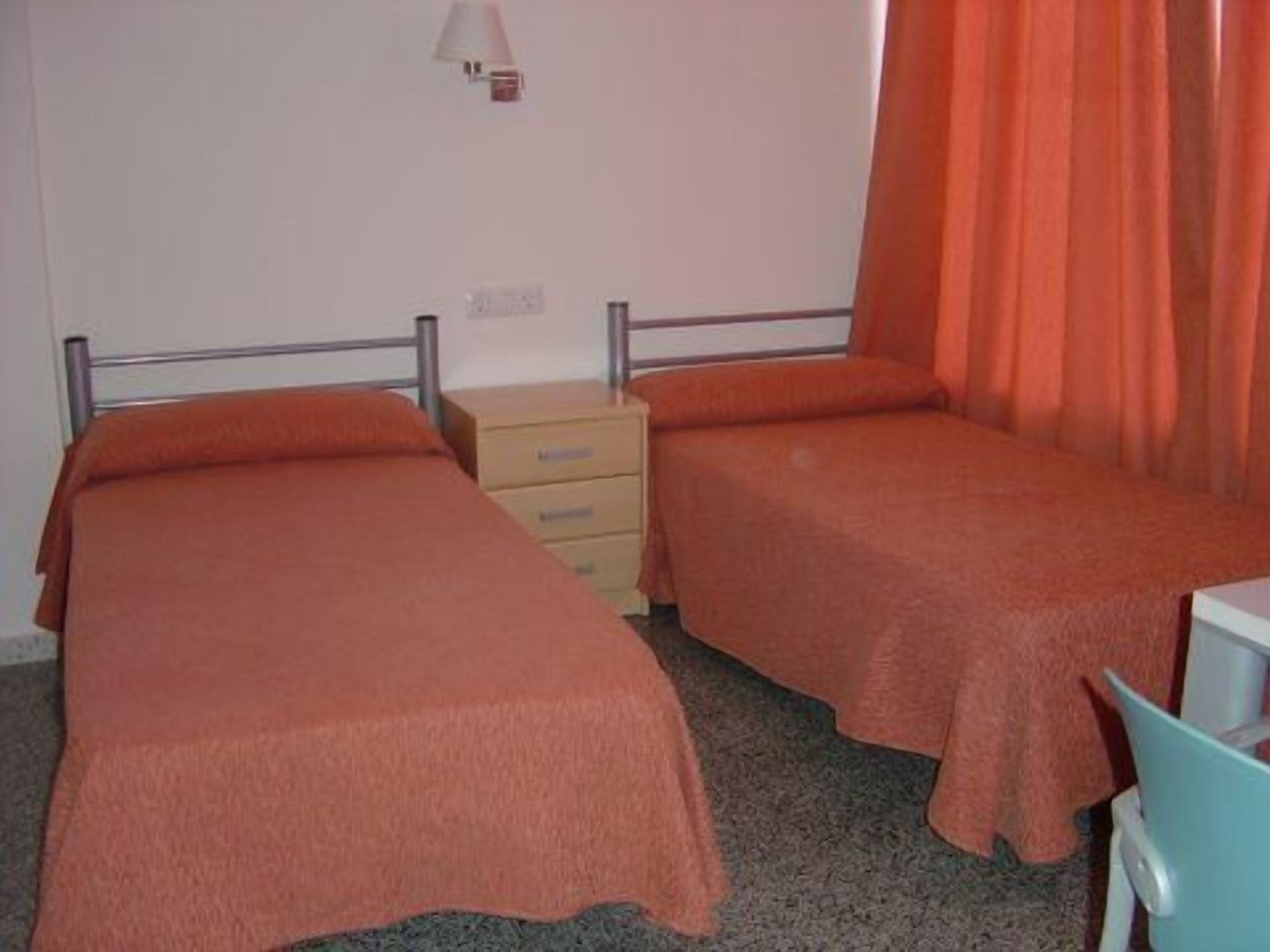 A twin room with two beds, a desk, a lamp, and a window with curtains.