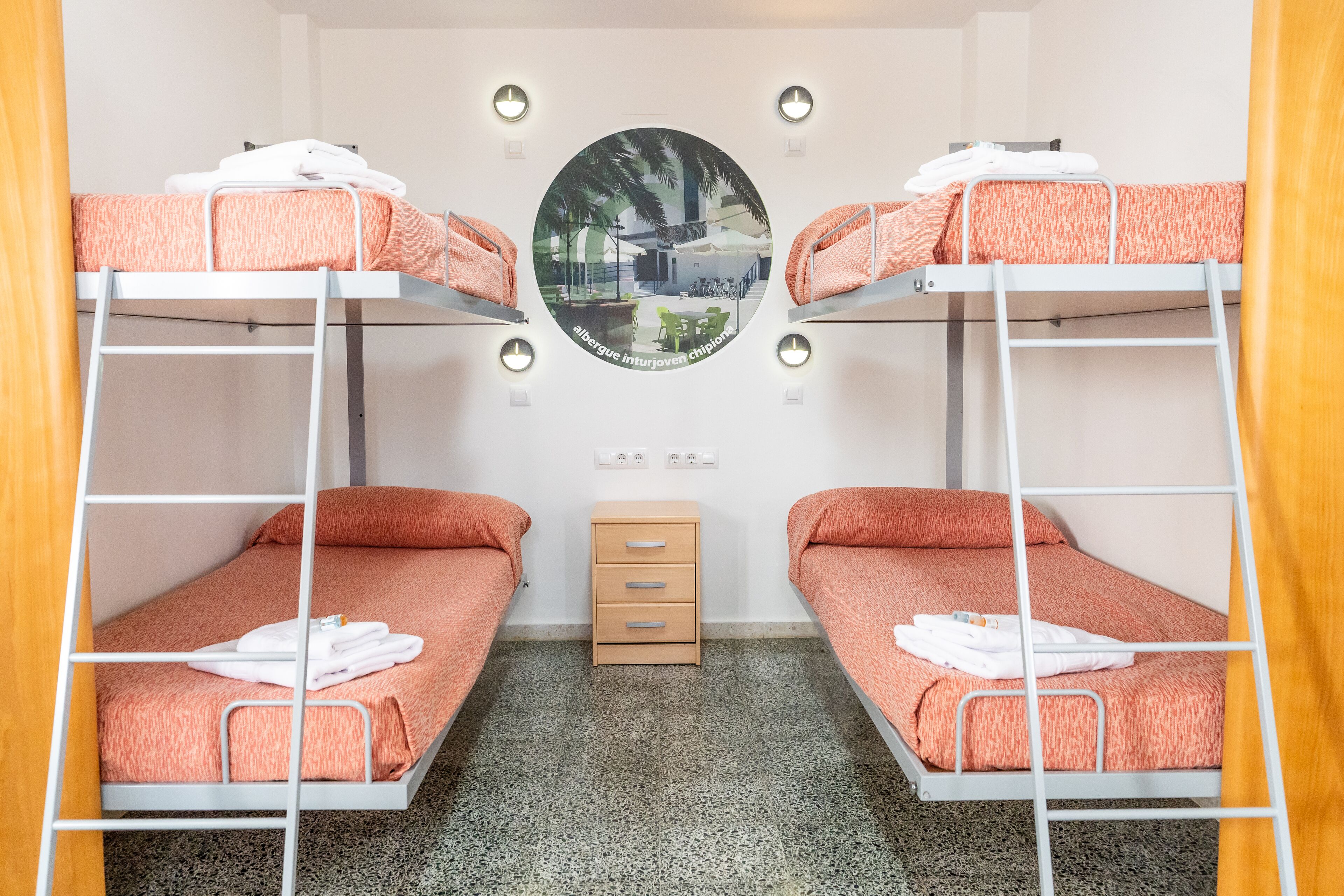 Habitación tipo dormitorio con camas literas, una mesita de noche de madera y un espejo circular fijado a la pared.