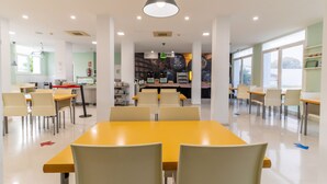 A cafeteria with yellow tables and chairs, white walls, and large windows. - Albergue Inturjoven Jerez de la Frontera - Hostel (Jerez de la Frontera)