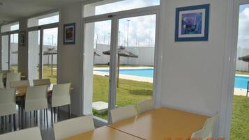 Un espace repas comprenant une table et des chaises, de grandes fenêtres et une vue sur une piscine.