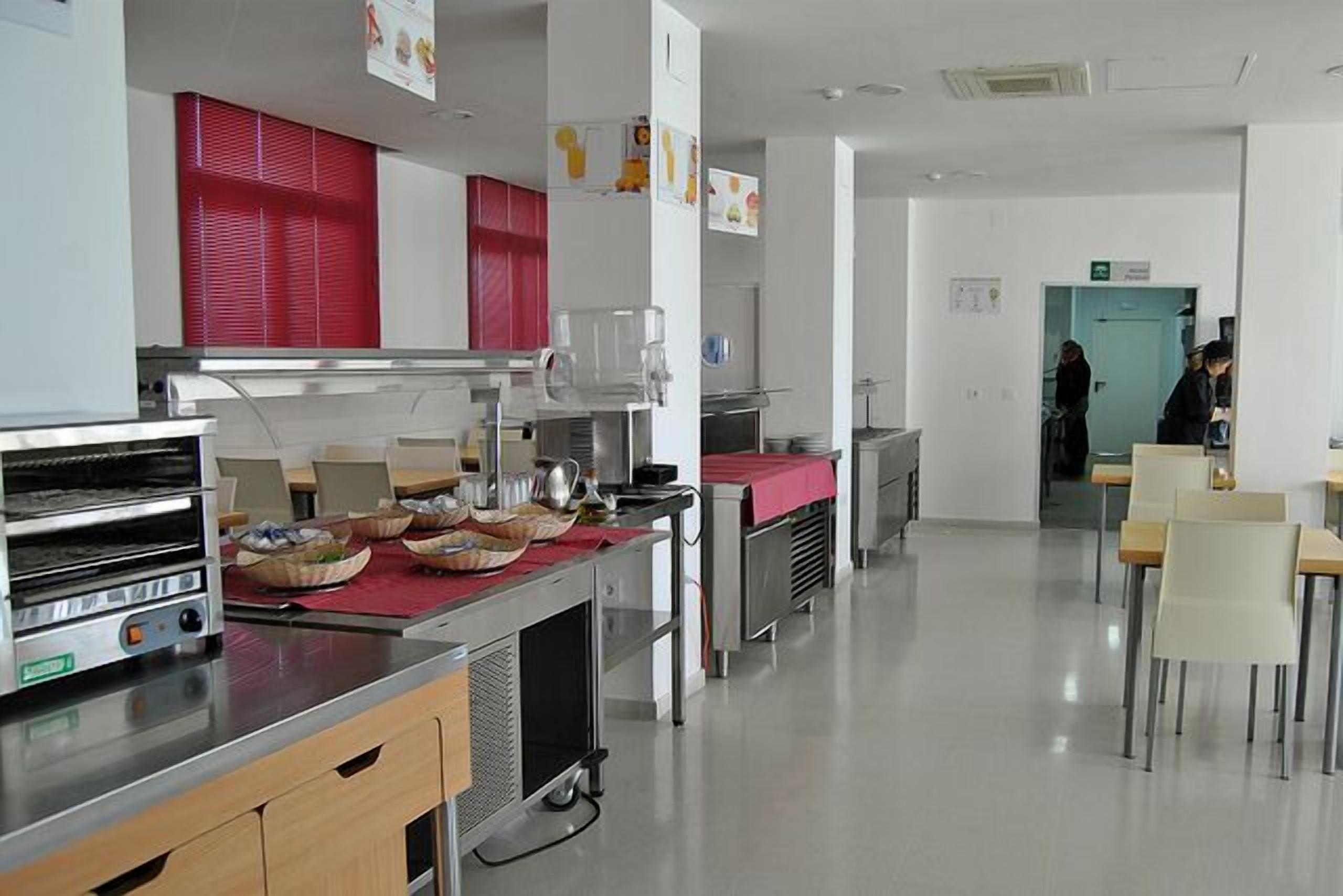 Una cocina moderna con electrodomésticos de acero inoxidable, encimera roja y un rincón de comedor con sillas y mesas.