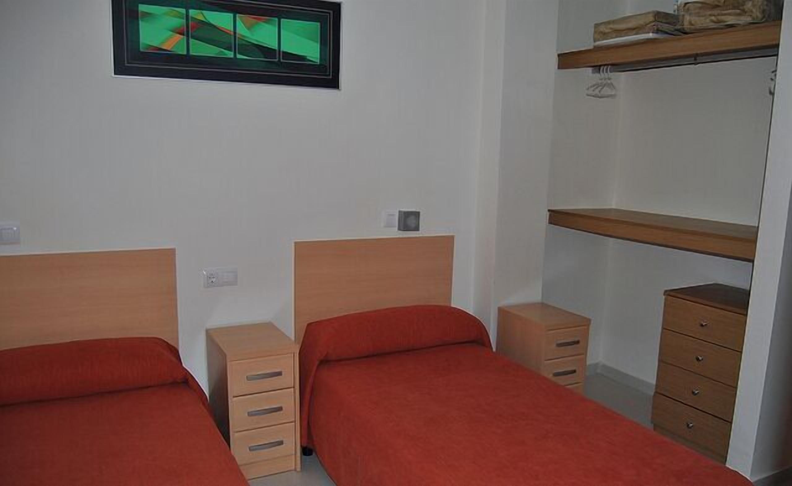 A bedroom with two single beds, a wooden dresser, a mirror, and a shelf with a bag.