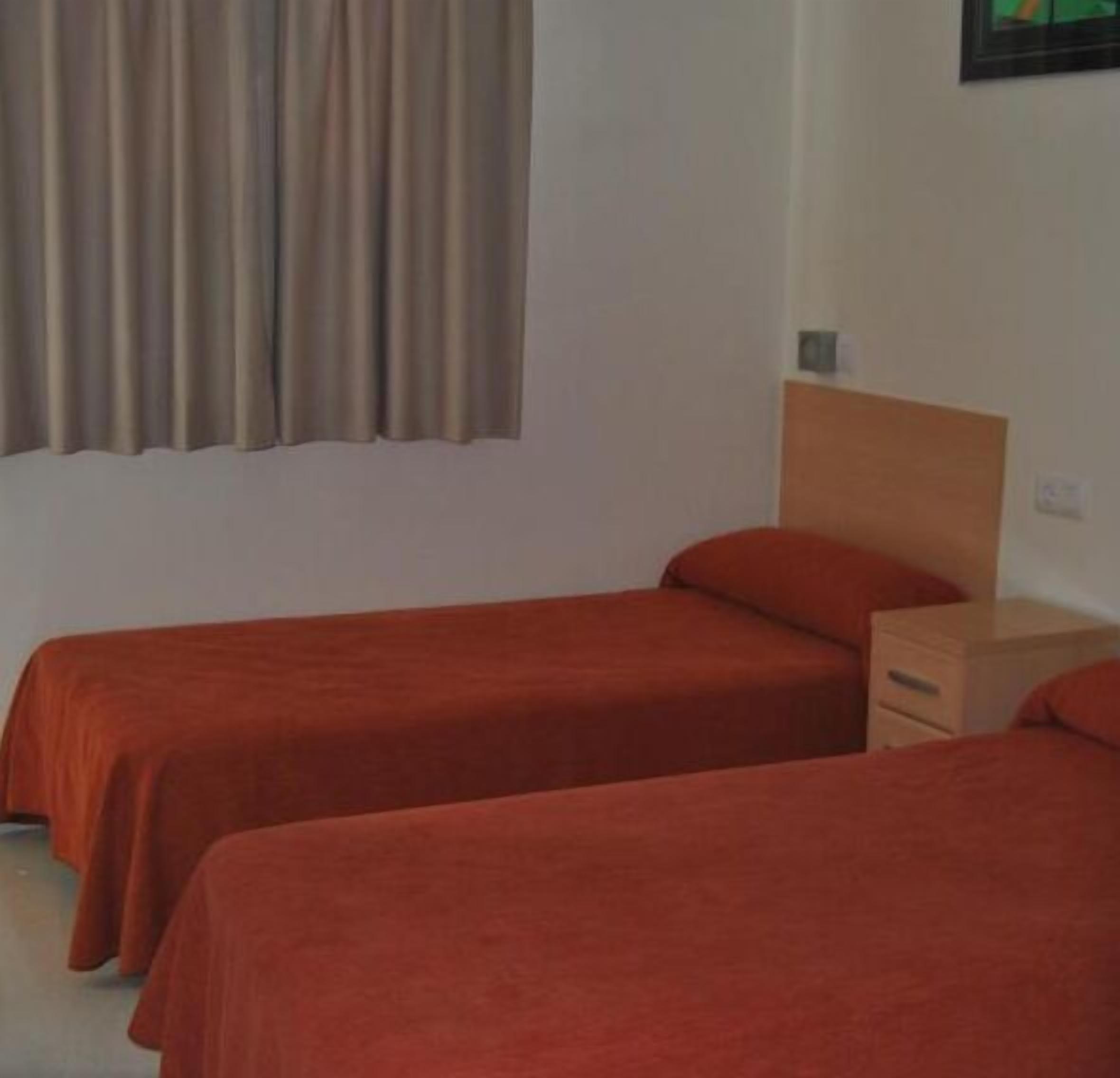 A room with two single beds, a wooden headboard, a nightstand, and a window with curtains.