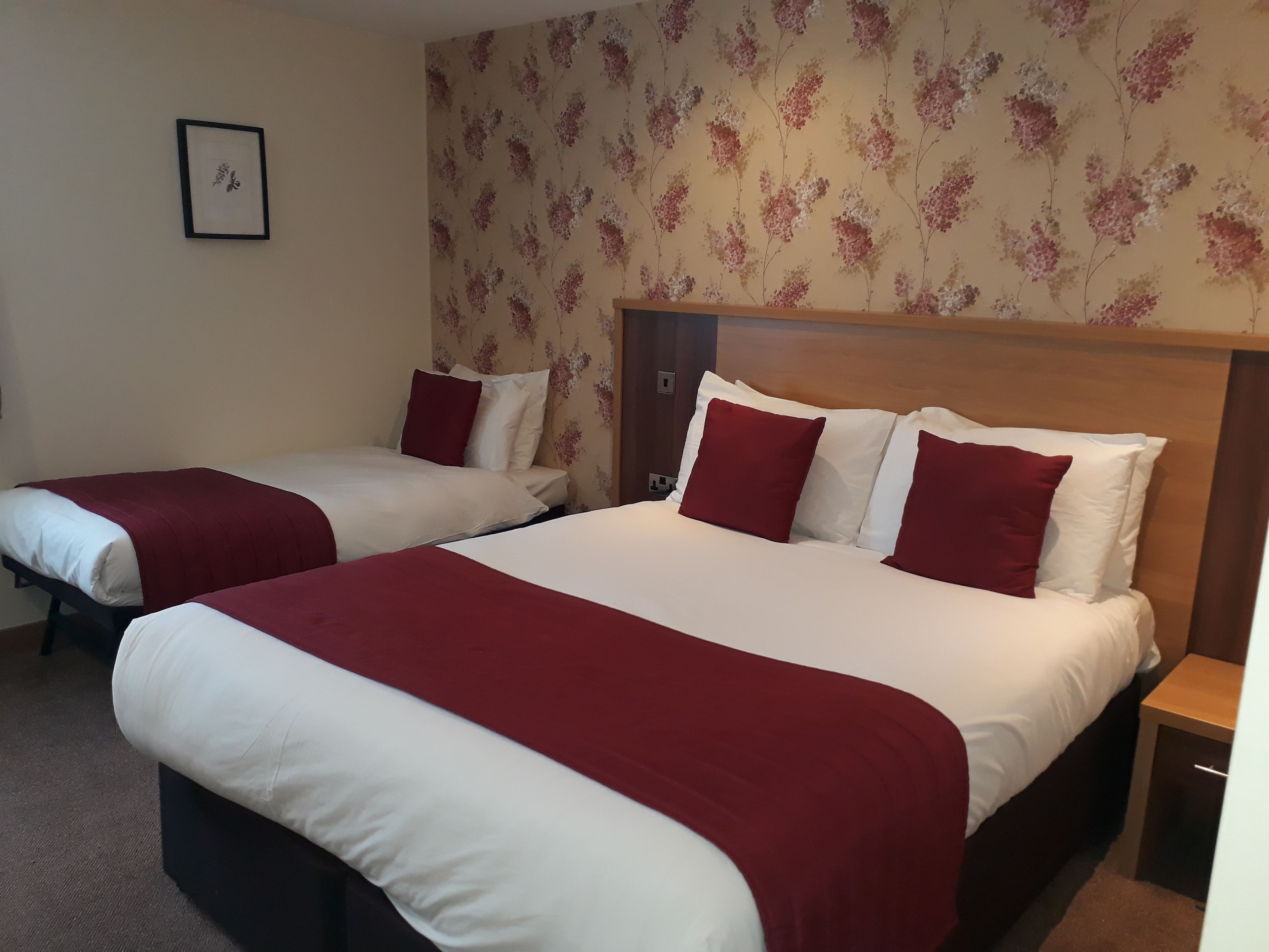 A hotel room with two beds, each with white and red bedding, and a floral wallpaper pattern.