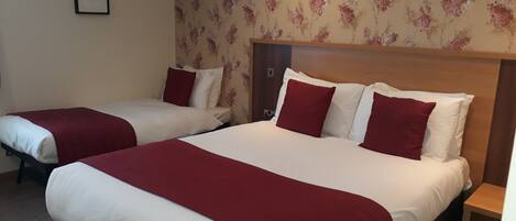 A hotel room with two beds, each with white and red bedding, and a floral wallpaper pattern.