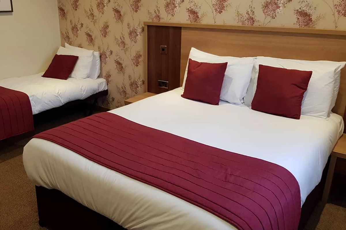 Dos camas individuales con ropa de cama roja y blanca, un cabecero de madera y un estampado de papel tapiz floral.