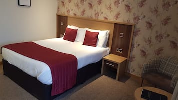 Una cama bien hecha con una colcha roja, un cabecero de madera y una mesita de noche con una lámpara.