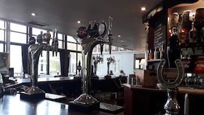 Una zona de bar con varias llaves de cerveza, una selección de botellas y un panel con la carta.