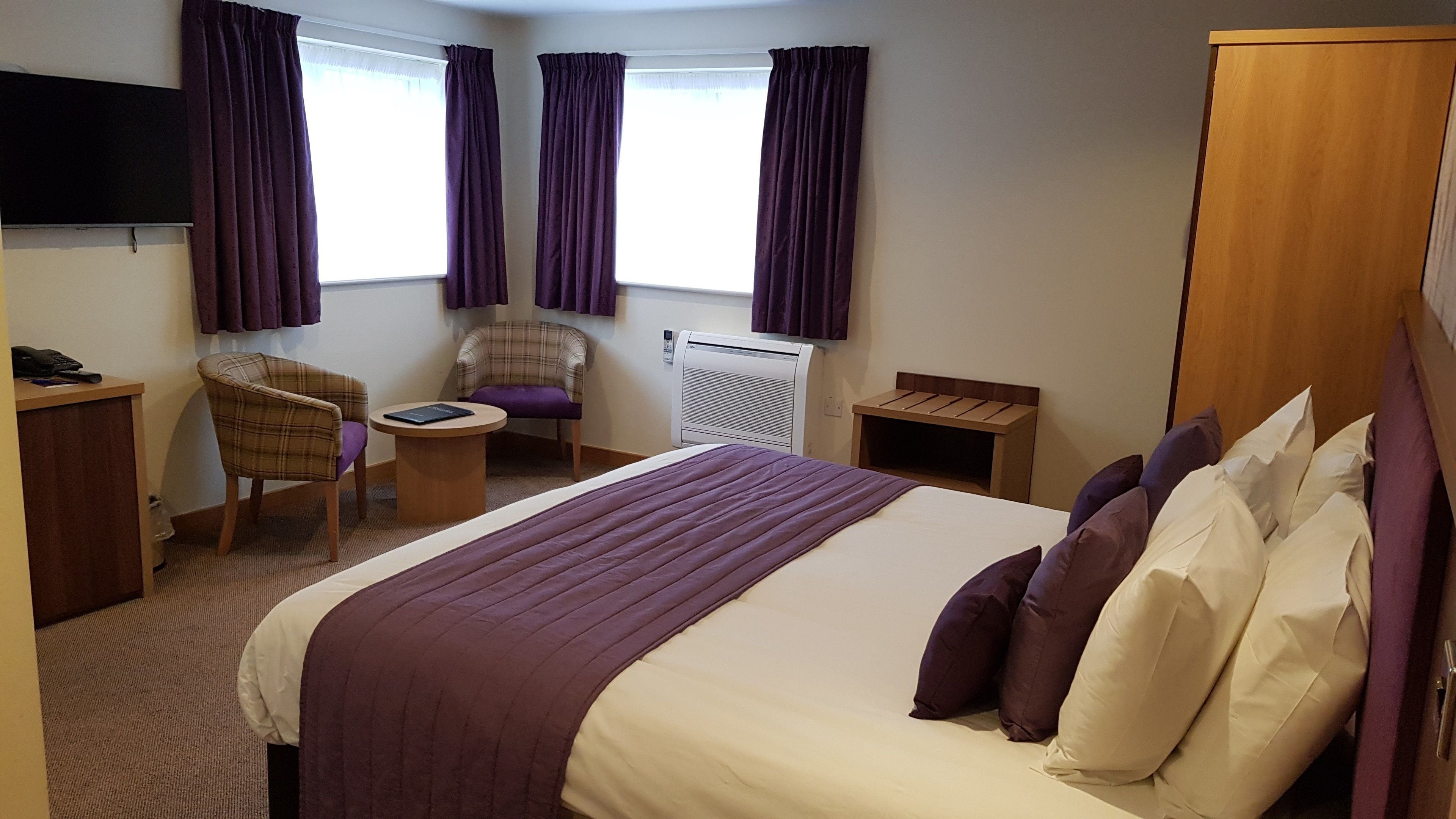 A hotel room with a bed, a desk, a chair, a small table, and a TV.