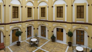 A courtyard with a central open space, surrounded by arched doorways and windows, and furnished with tables and chairs. - Albergue Inturjoven Córdoba - Hostel (Córdoba)
