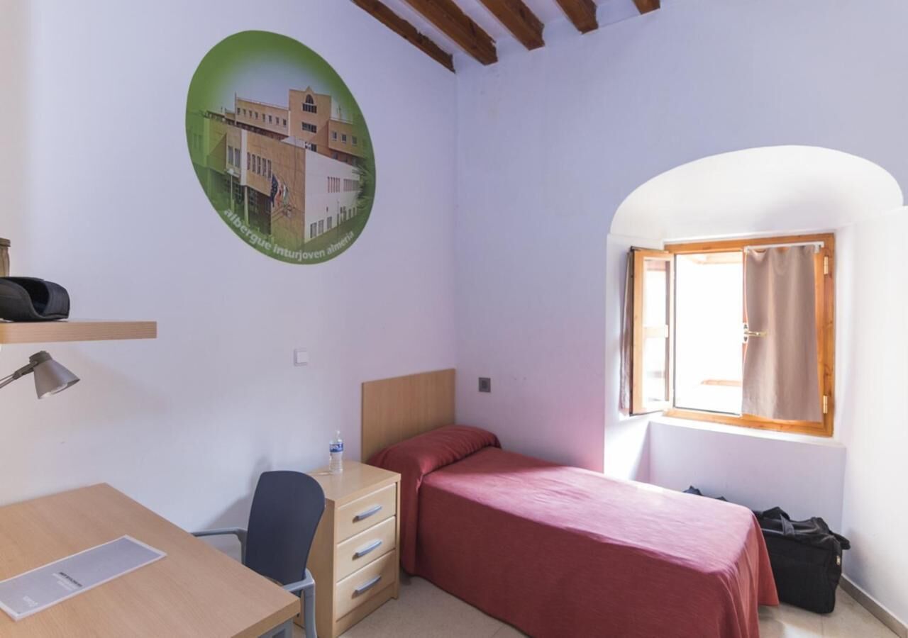 Un dormitorio con cama, escritorio, silla y ventana con cortinas.