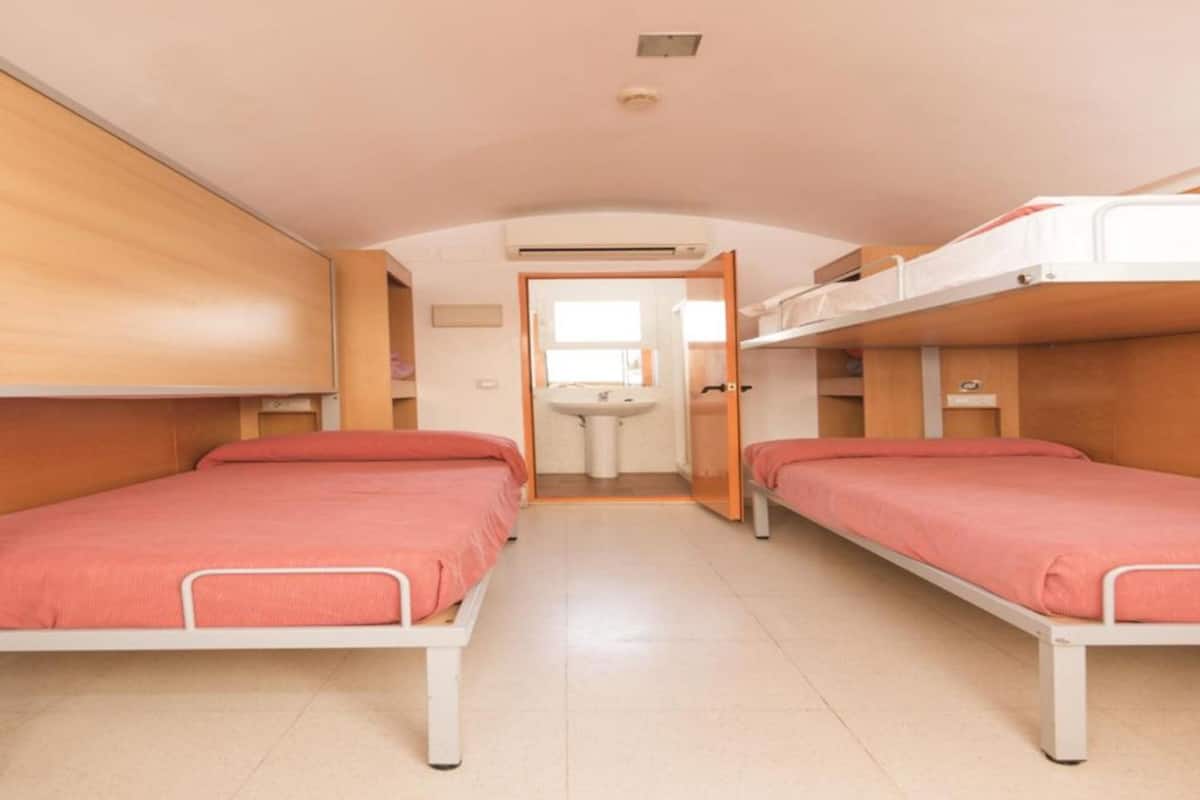 Ein kleines Zimmer mit zwei Etagenbetten, einem kleinen Waschbecken und einer Tür zu einem weiteren Bereich.