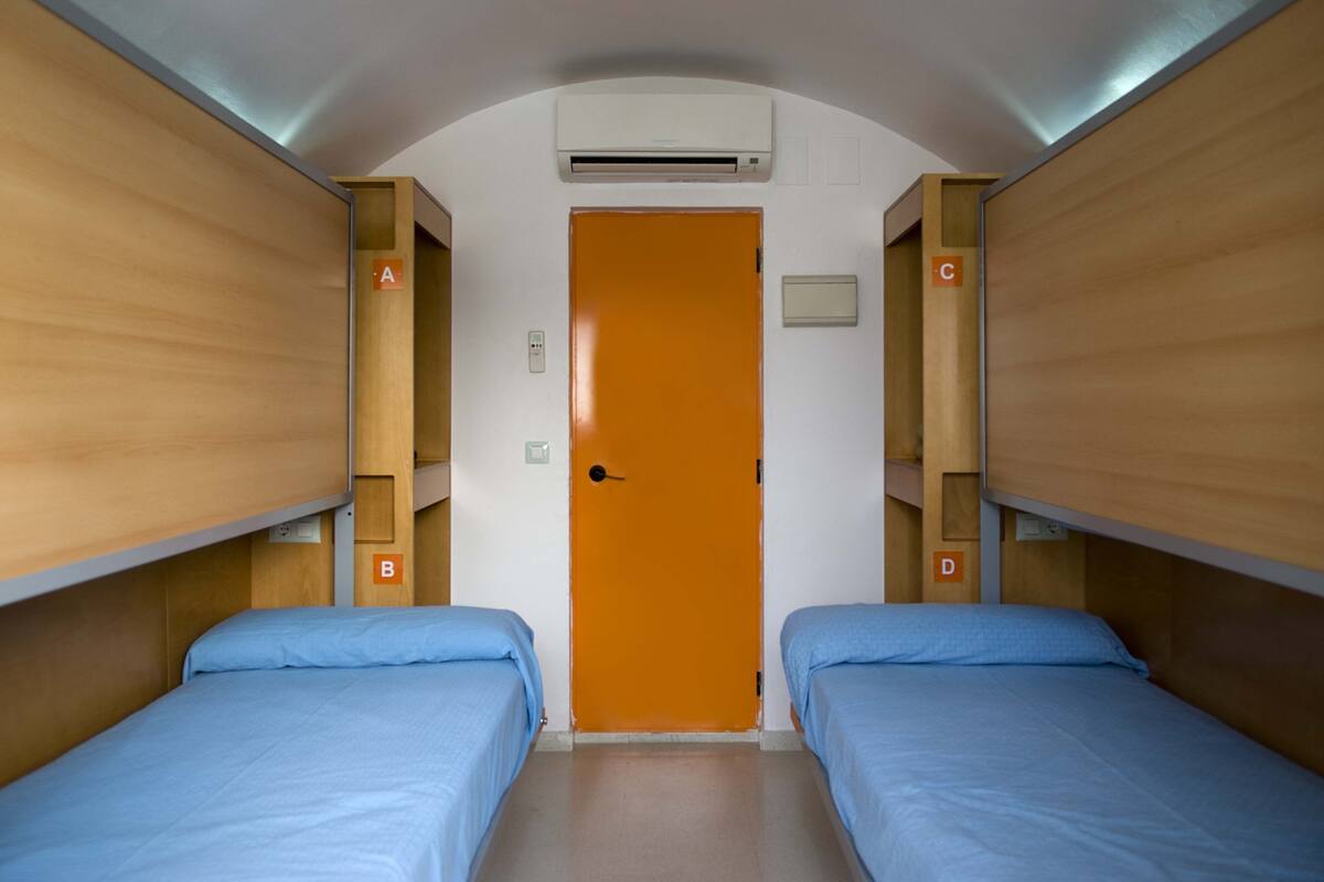 Ein Zimmer mit zwei Betten, einer orangen Tür und einer Klimaanlage an der Decke.