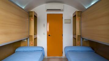 A room with two beds, an orange door, and an air conditioning unit on the ceiling.