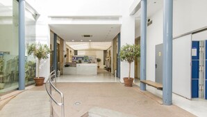 A modern hotel lobby with a central reception desk, potted plants, and a staircase leading to upper floors. - Albergue Inturjoven Córdoba - Hostel (Córdoba)