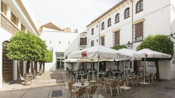 An outdoor café with tables and chairs, white umbrellas, and a cobblestone path. - Albergue Inturjoven Córdoba - Hostel (Córdoba)