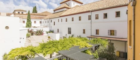 A courtyard with white buildings, a tiled roof, and greenery.