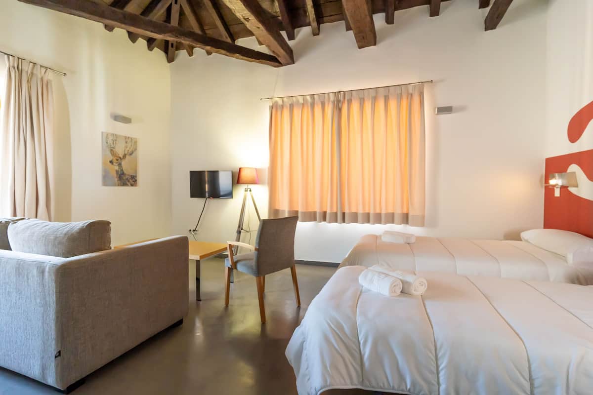 A hotel room with a sofa, a desk, a chair, and two beds.