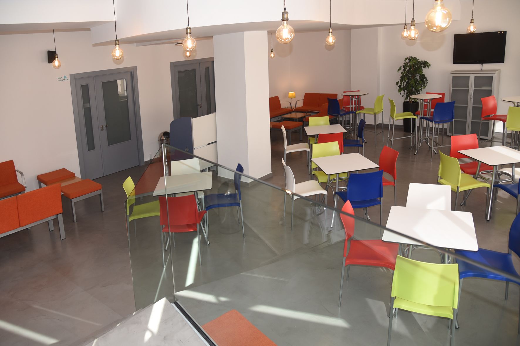 A modern dining area with glass partitions, colorful chairs, and pendant lighting.