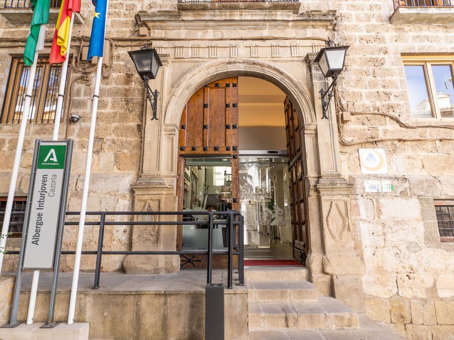A stone building entrance with a wooden door, a sign indicating a location, and flags.